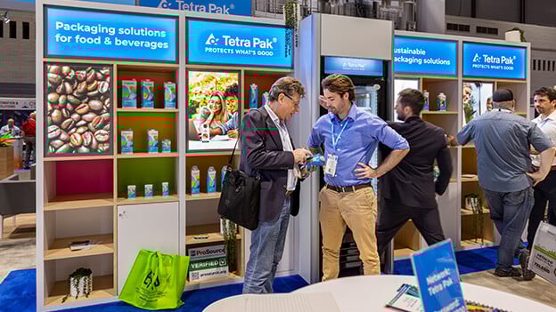 Two professionals engaged in conversation at the Tetra Pak booth during the Pack Expo trade show